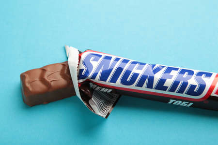 Nikolaev, Ukraine - December 19, 2021 Snickers chocolate bar on blue background. Snickers is a brand name chocolate bar made by the American company Mars. Top view.のeditorial素材
