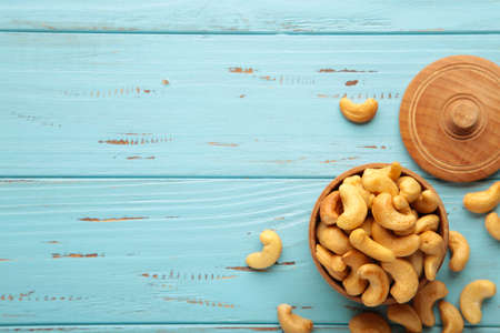 Cashew nuts on wooden bowl on blue background. Vertical photo.の写真素材
