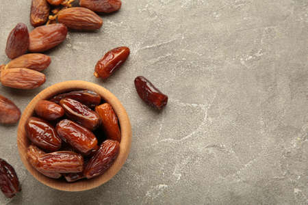 Wooden bowl of dried dates on gray wooden background. Branch with dates on gray.の写真素材