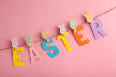 Inscription Easter on pink background, a rope with clothespins. The concept of postcards for the...