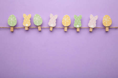 Easter eggs and bunnies on clothespin on purple background with copy space. Top view