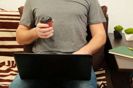 Businessman with coffee cup working at home with a laptop on sofa. top view