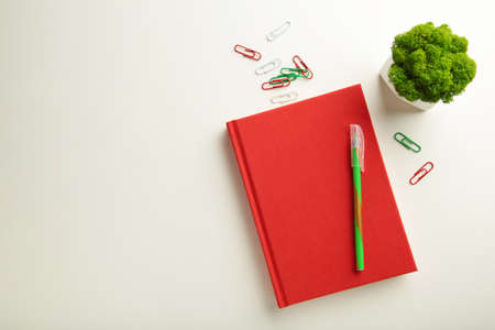 Red notebook with green plant on white background with copy space. top view