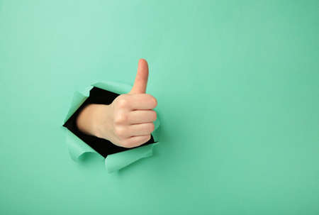 Female hand with positive gesture through the mint paper. top viewの写真素材