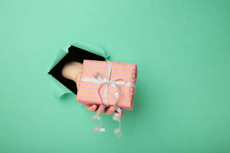 Female hand with gift box punching through the mint paper. top viewの写真素材