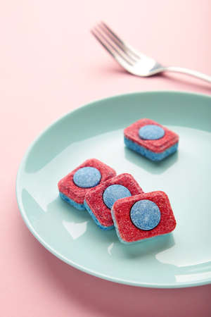 Dishwasher detergent tablet with fork and dishes on pink background. top view