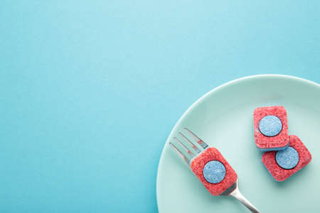 Dishwasher detergent tablet with fork and dishes on blue background. top view
