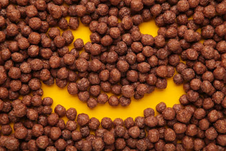 Smile made of chocolate corn balls on yellow background.