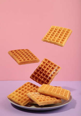 Belgian waffles flying in the air on a pasel pink background. Waffles in plate. creative food concept. vertical photoの写真素材
