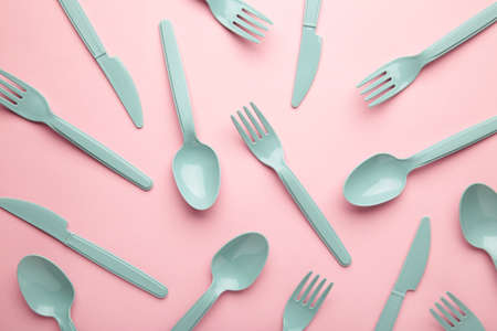 Many blue plastic forks, spoons and knives on pink background with copy space