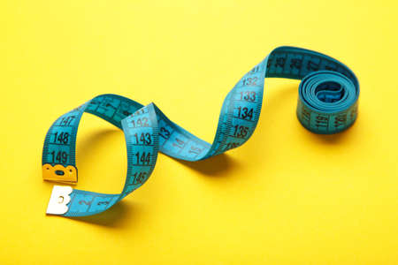 Blue plastic measure tape with metric scale over on color yellow background. top view. Diet concept