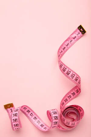 Pink plastic measure tape with metric scale over on color pink background. top view. Diet conceptの写真素材