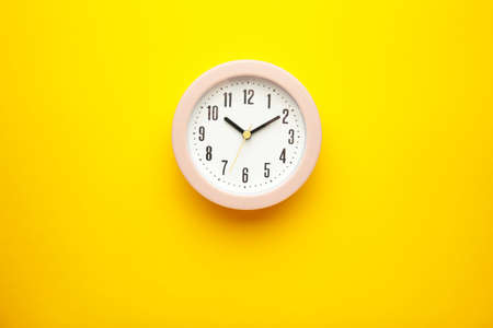 Pink clock on yellow background. top view. vertical photoの写真素材