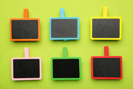 Blank wooden chalk plate on clothes pins on green background. top viewの写真素材