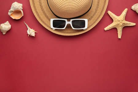 Travel, vacation concept. Hat with sunglasses and sea shells on red background. Space for text. top...