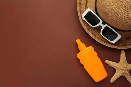 Travel, vacation concept. Hat with sunglasses and sunscreen on brown background. Space for text. top...