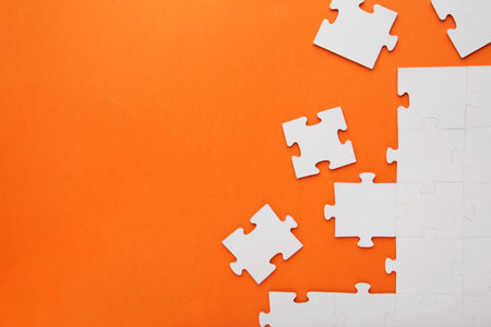 Unfinished white jigsaw puzzle pieces on orange background. top view.の写真素材