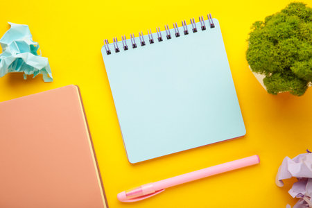 A notebook with a blank page and pen on yellow background. Copy space, layout, mockup. top view