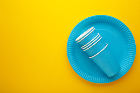 Eco-friendly disposable utensils made of craft paper on yellow background. Blue plates and paper cups. top viewの写真素材