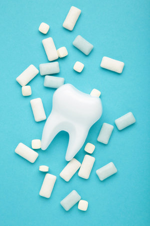 White healthy tooth model and heap of chewing gums on blue background. Concept of oral dental...