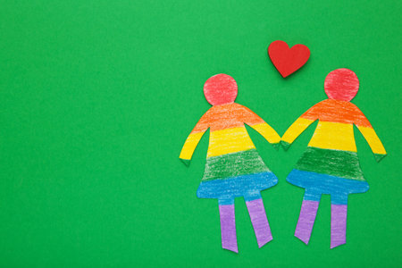 Paper women cut from paper and painted in LGBT colors with red heart. Concept of LGBT on green. Space for text. top view.の写真素材