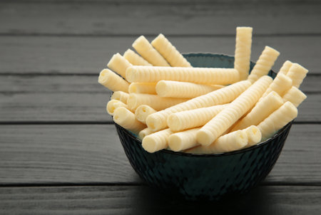 Delicious milk wafer rolls on bowl on black background. top view