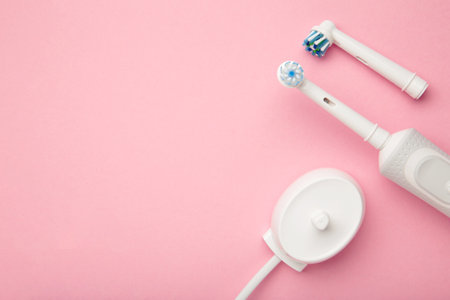 Modern electric toothbrush with spare heads and charger on pink background. Space for textの写真素材
