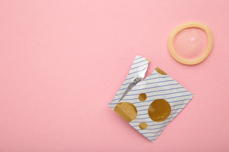 Opened condom in pack on pink background. A condom use to reduce the probability of pregnancy or...