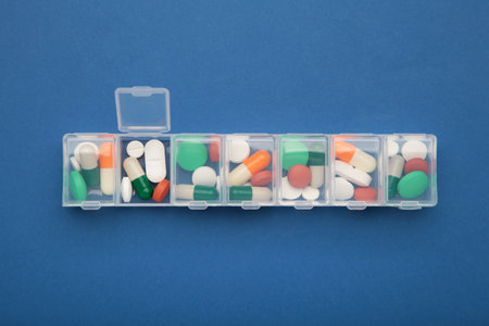 Daily pill box with medications and nutritional supplements on dark blue. top view