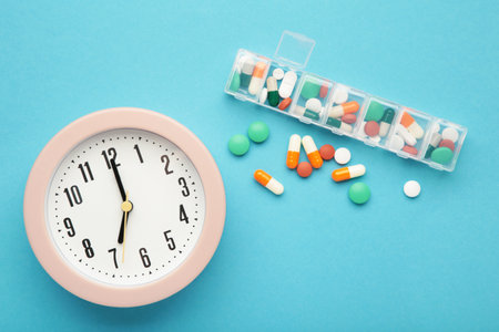 Pink clock, tablets and weekly tablet organizer on blue background. Concept of time of taking the pills. top viewの写真素材