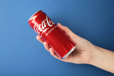 Mykolaiv, Ukraine - May 2, 2023: Woman holding Coca-Cola can on blue background. top view