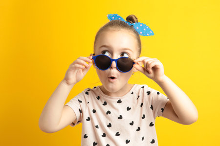 Portrait of surprised cute little toddler girl in sunglasses. Child with open mouth having fun on yellow background. Looking at camera. Wow funny face. Top viewの写真素材