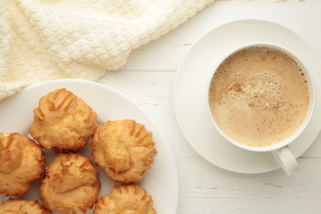 Homemade profiteroles with cream on plate with cup of coffee on white background. Fresh baked golden...