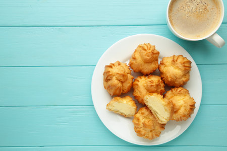 Homemade profiteroles with cream on plate with cup of coffee on blue wooden background. Fresh baked golden profiterole. Top view.の写真素材