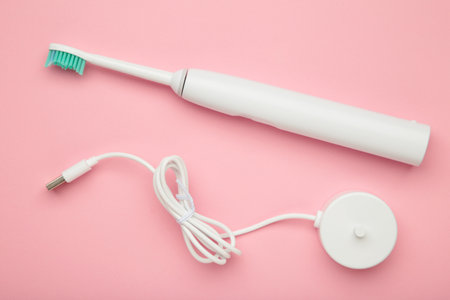 Smart electric toothbrush on pink background. Charges through powerbank and is controlled by the...