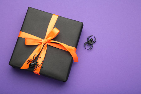 Happy Halloween holiday concept. Flat lay gift box with spiders on violet background. Halloween...