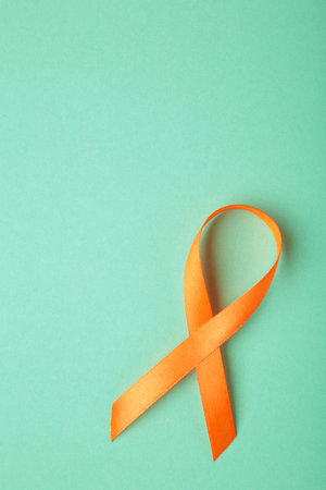Orange ribbon on mint background. Healthcare and medicine concept. Multiple Sclerosis awareness. Leukemia awareness. Empty text space. Top viewの写真素材