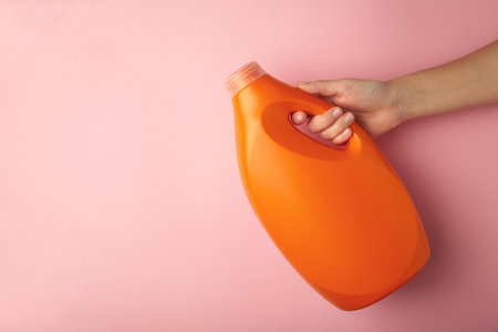 Hand with liquid laundry detergent bottle, cleaning soap for cloth on pink background. Top viewの写真素材