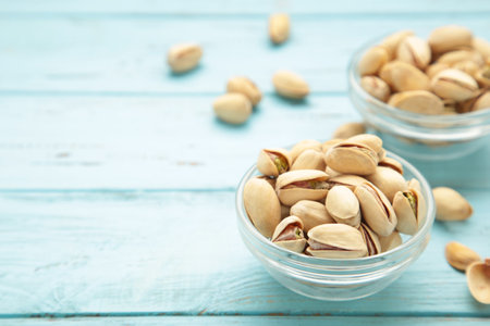 Bowl with pistachios on blue wooden background. Space for text. Top view