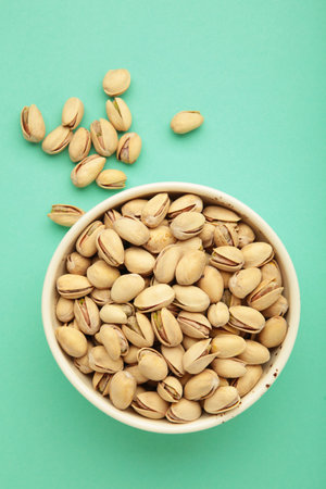 Bowl with pistachios on mint background. Vertical photo. Top view