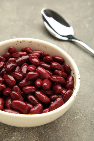 Red beans in bowl and spoon on gray background. Vertical photo