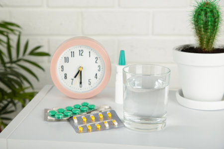 Pink alarm clock with glass of water and blister packages of pills on light table background. Top viewの写真素材