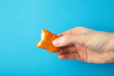 Chicken nugget with a bite taken in hand on a blue background. Top viewの写真素材