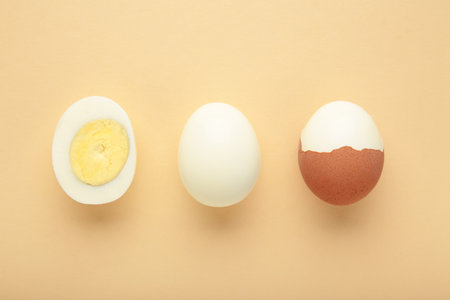 Whole white egg and halved boiled egg with yolk on beige background. Top view.の写真素材