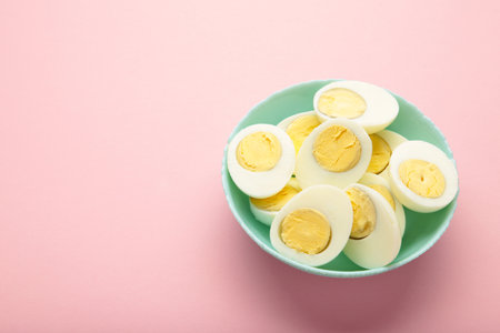 Halved boiled egg with yolk on plate on pink background. Top view.