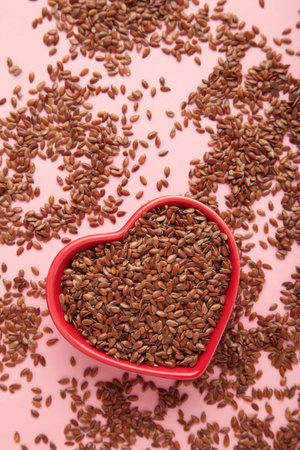 Healthy food. Flax seeds in red heart shaped bowls on pink background. Top viewの写真素材