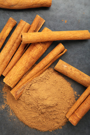 Cinnamon sticks with powder on dark background. Vertical photo