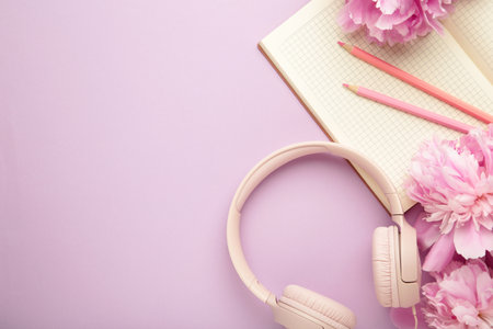 Modern pink headphones with flowers peonies and notebook on purple background. Top viewの写真素材
