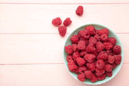 Raspberries in mint bowl on pink background. Space for text. Top viewの写真素材