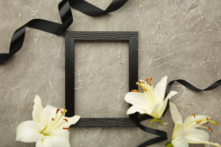 Beautiful lily flower with blank frame and black funeral ribbon on gray concrete background.の写真素材